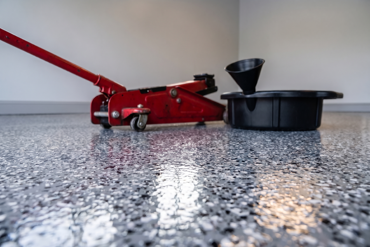 Rolling floor jack and a plastic drain pan resting on a glossy gray flake garage floor