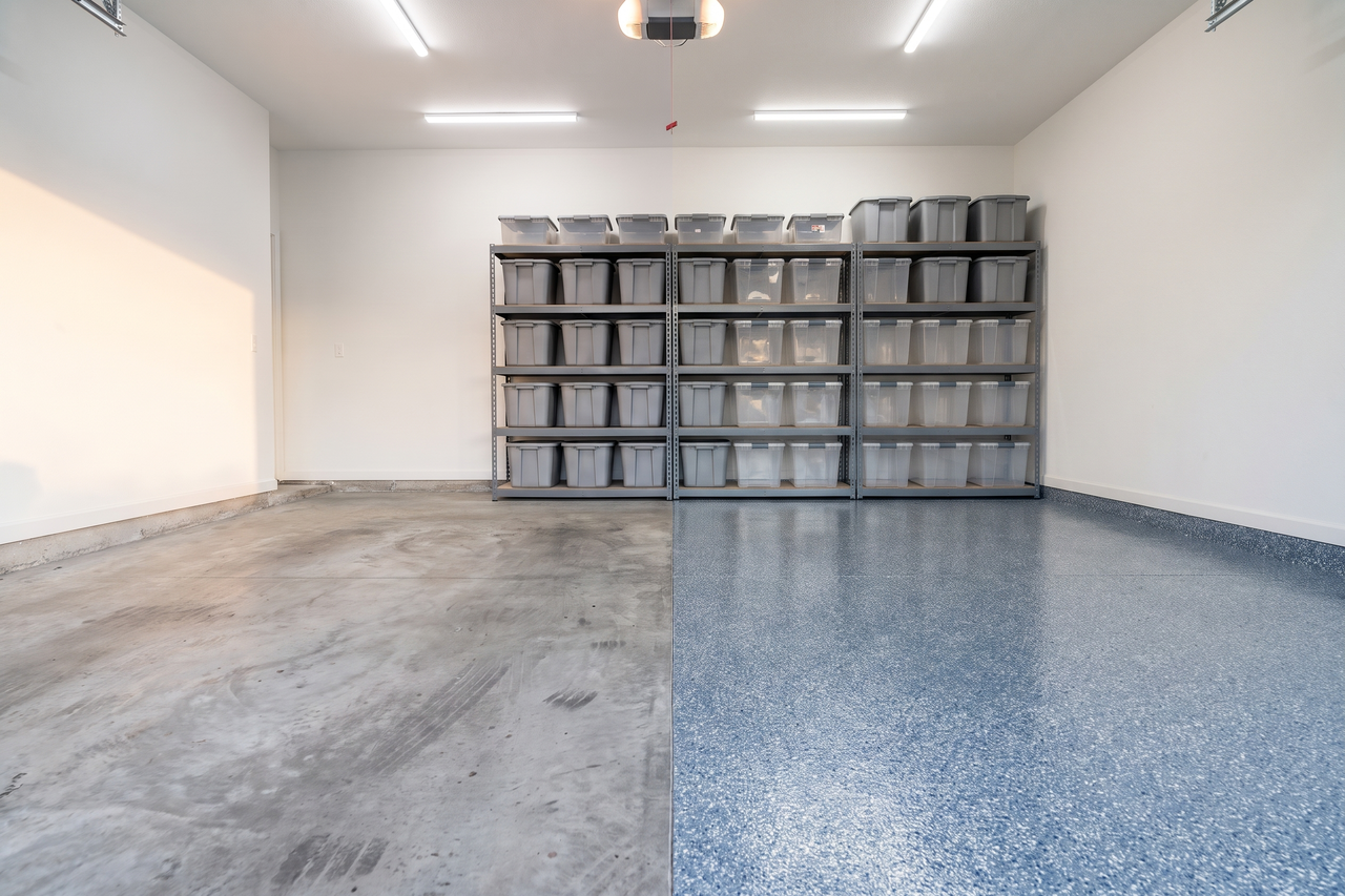 Illustrative before-and-after example of a two-car garage with blotchy, tire-marked concrete on one side and a glossy blue-gray and white flake floor on the other